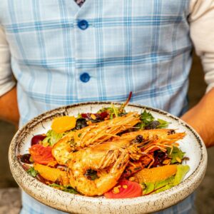 A waiter presenting a delicious shrimp and vegetable salad on a ceramic plate.