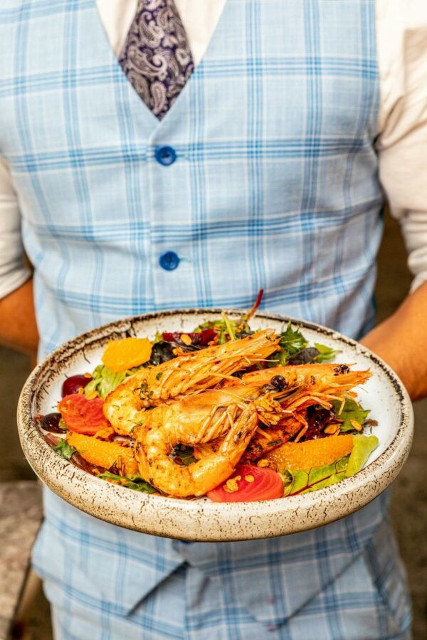 A waiter presenting a delicious shrimp and vegetable salad on a ceramic plate.